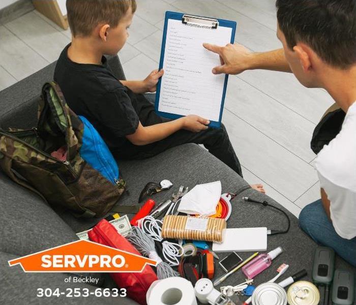A father and son review a disaster supply checklist while packing emergency supplies. 